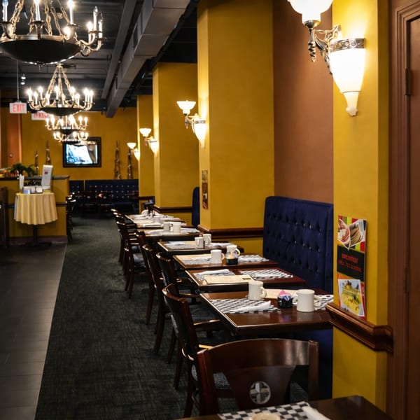 A long, narrow restaurant dining room with dark wood tables, blue booths, and yellow walls.