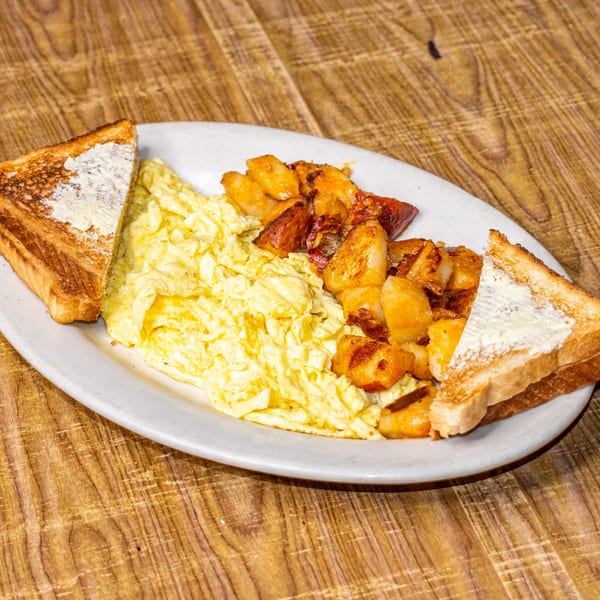 A breakfast plate with scrambled eggs, home fries, and two slices of buttered toast on a wooden table.