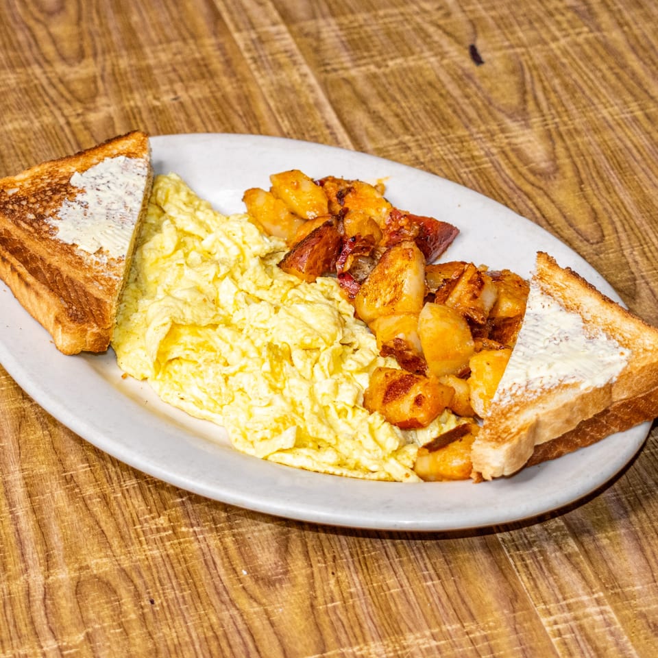 A breakfast plate with scrambled eggs, home fries, and two slices of buttered toast on a wooden table.