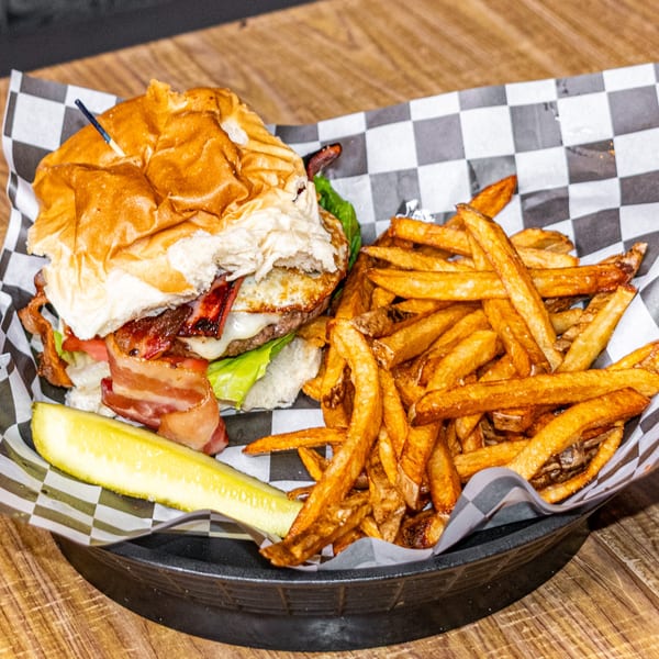 A bacon cheeseburger with lettuce, tomato, and a pickle spear, served with fries.