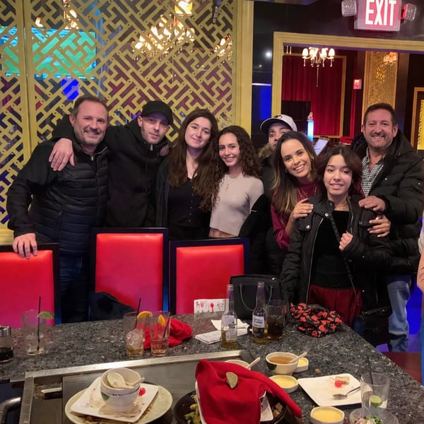 Group of eight people smiling at a hibachi table with drinks and finished plates.
