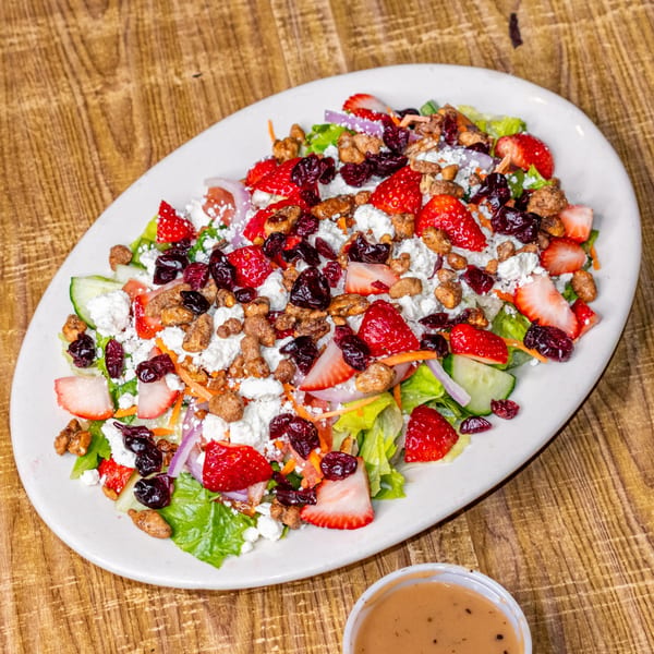 A vibrant salad with strawberries, cranberries, nuts, and feta cheese on a white plate.