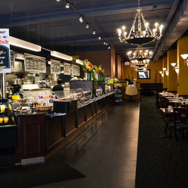 A restaurant interior with a long food counter, menu boards, and dining tables with chandeliers.