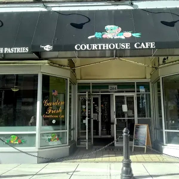 Exterior view of Courthouse Cafe, a restaurant with a black awning and large windows, on a sunny day.
