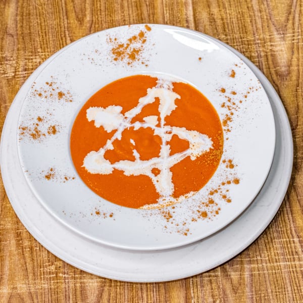 Vibrant orange soup with a white cream swirl and sprinkled spices, served on a white plate.