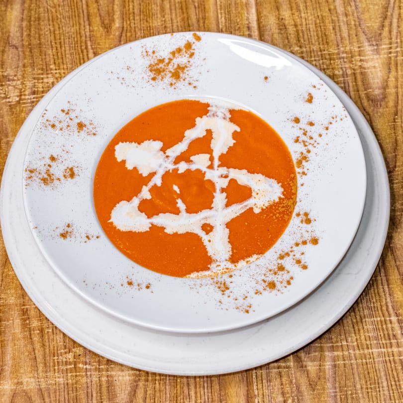 Vibrant orange soup with a white cream swirl and sprinkled spices, served on a white plate.