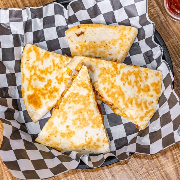 Four golden-brown quesadilla wedges with melted cheese and fillings, served in a basket with checkered paper.