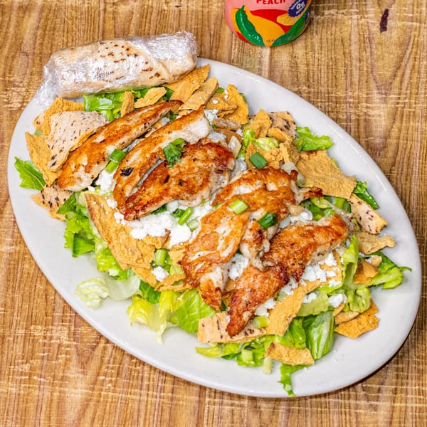 Grilled chicken salad with lettuce, tortilla strips, feta cheese, and green onions, with a wrapped pita.