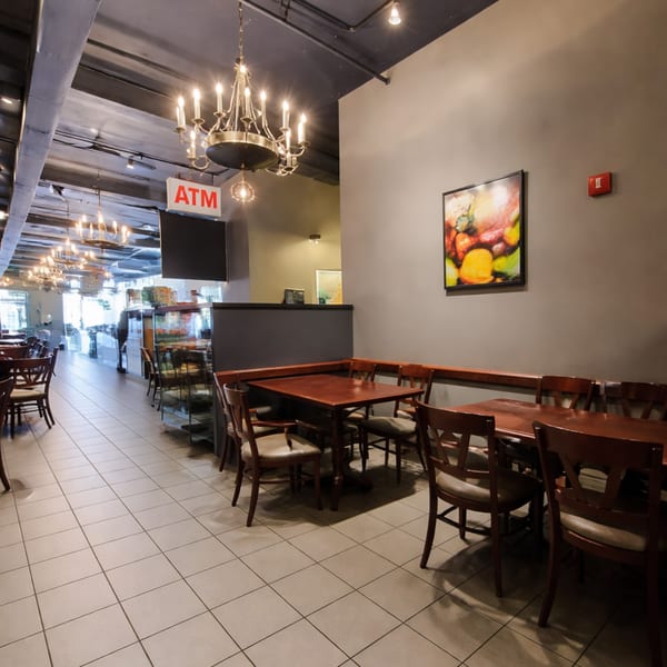 Restaurant interior with dark wood tables and chairs, chandeliers, and an ATM sign.