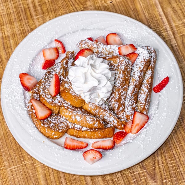 Golden French toast topped with whipped cream, fresh strawberries, and powdered sugar on a white plate.